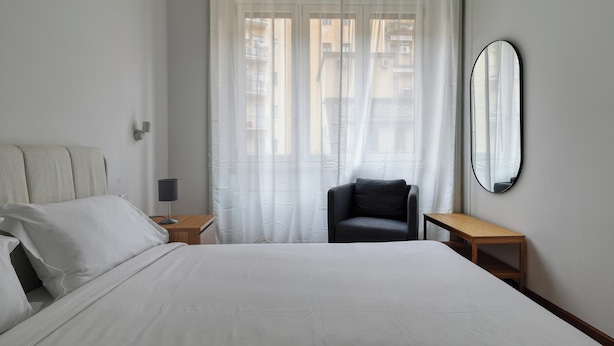 A bedroom with a large bed, a chair, a small table, and a mirror on the wall. - JOIVY Welcoming 3BR Flat in Milan Centre (Milan)