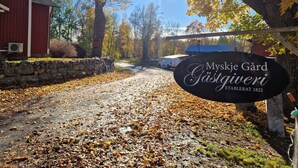 A sign for 'Myskje Gård Gästgiveri' with a stone wall and a red building in the background. - Myskje Gård Äventyr (Soderala)