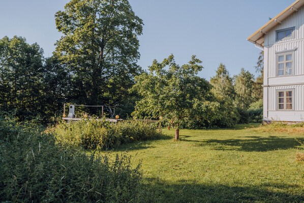 A white building with a balcony and a garden with trees and grass. - Myskje Gård Äventyr (Soderala)