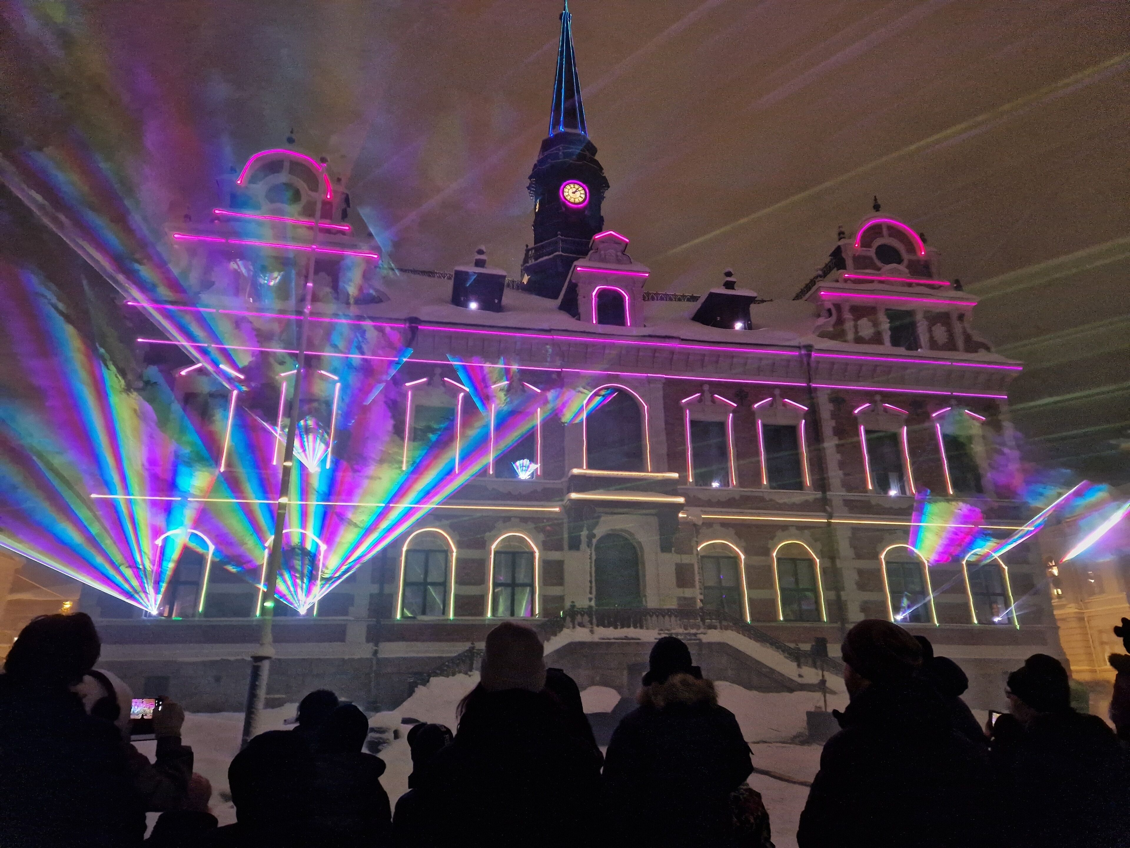 A historic building with arched windows and a clock tower, illuminated by colorful lights.