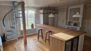 A kitchen with a wooden island, bar stools, a spiral staircase, and hanging pendant lights. - Myskje Gård Äventyr (Soderala)
