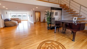 Un vaste salon agrémenté d’un magnifique piano à queue, d’un escalier et d’une grande fenêtre donnant sur une étendue d’eau.