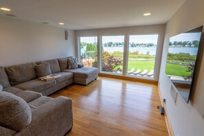 A modern living room with a sectional sofa, a flat-screen TV, and a large window offering a view of a lake and greenery.