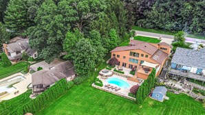 Une grande maison avec une piscine, entourée d’une pelouse bien entretenue et d’arbres.