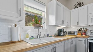 A modern kitchen with white cabinets, a wooden countertop, a sink, a window with plants, and various kitchen appliances. - Secluded Guest House in beautiful setting (Austin)