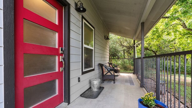 A porch with a red door, two windows, a metal trash can, and a blue planter with yellow flowers. - Secluded Guest House in beautiful setting (Austin)