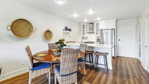 A modern kitchen with white cabinets, a stainless steel refrigerator, and a dining area with wicker chairs and a wooden table. - Sunset Rentals- 682 Mariners Way (Hilton Head Island)