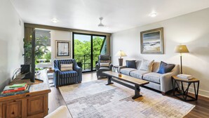 A spacious living room with a large window, a sofa, a chair, a coffee table, and a TV. - Sunset Rentals- 682 Mariners Way (Hilton Head Island)