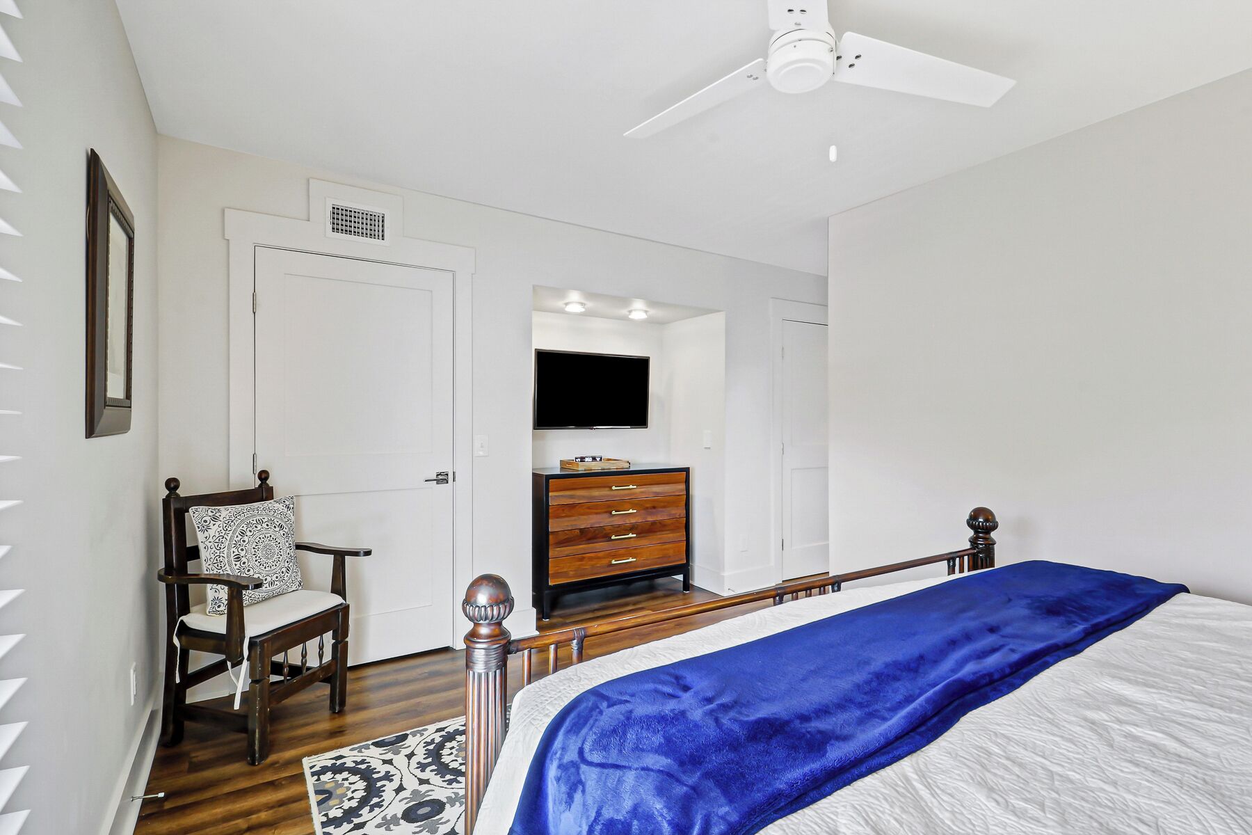 A bedroom with a bed, a dresser, a chair, a ceiling fan, and a television.