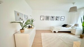A modern bedroom with a bed, bedside tables, a sofa, a large rug, and wall-mounted artwork.
