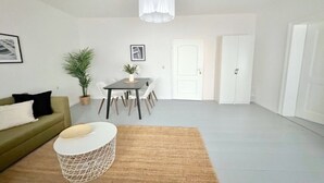 A modern living room with a sofa, a coffee table, a dining table with chairs, a potted plant, and a white door. - Arbio Monteurzimmer Rüdersdorf 4 people (Rüdersdorf bei Berlin)