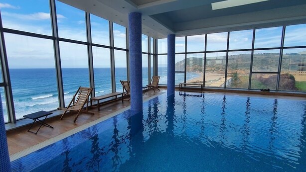 Una piscina interior con grandes ventanales que ofrecen vistas al océano.