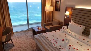 Habitación de hotel con una cama grande, una silla, un escritorio y vista al océano.