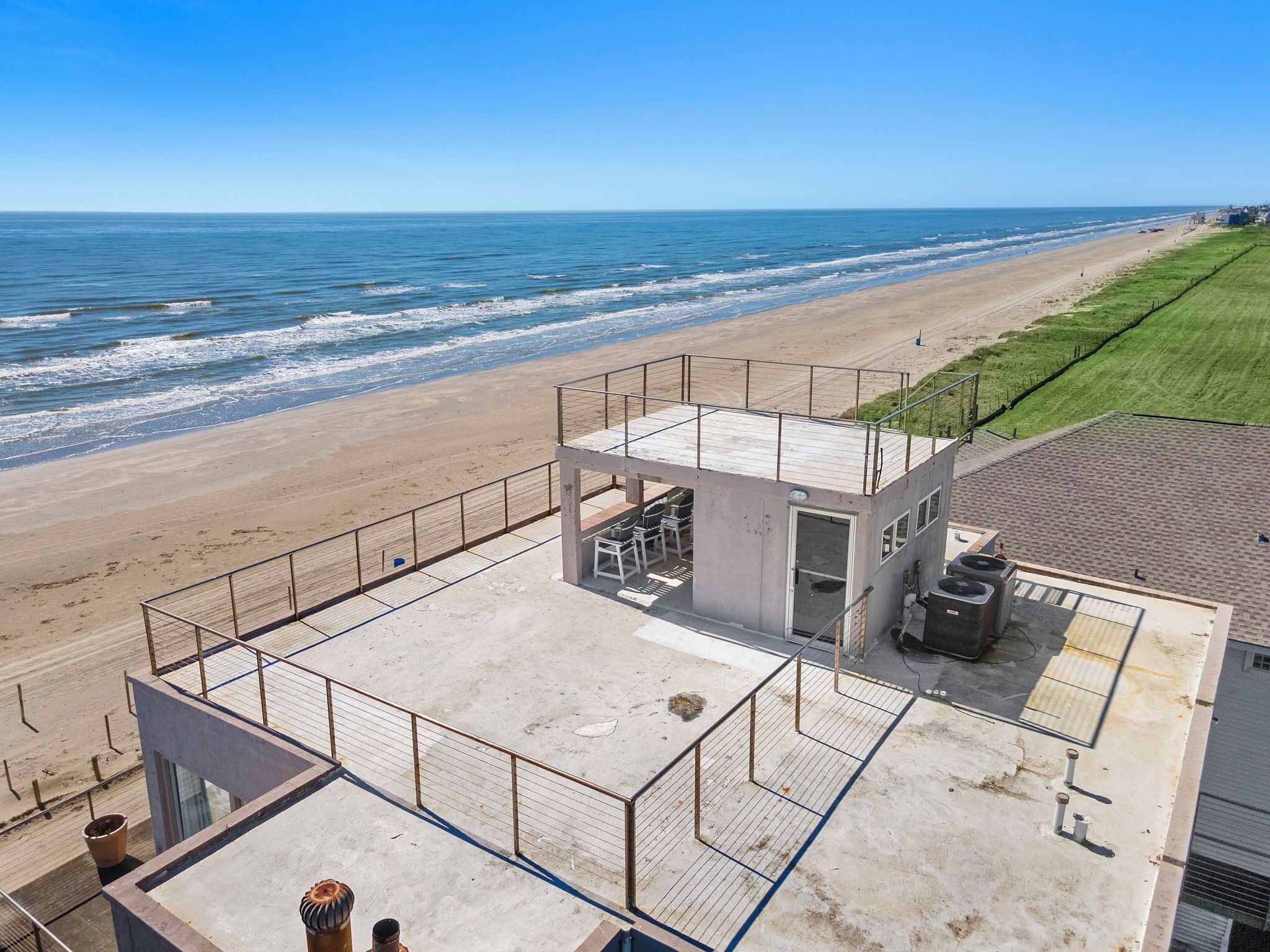 Ein Gebäude direkt am Strand mit einer umzäunten Terrasse, einem kleinen Pool und einem Rettungsturm.