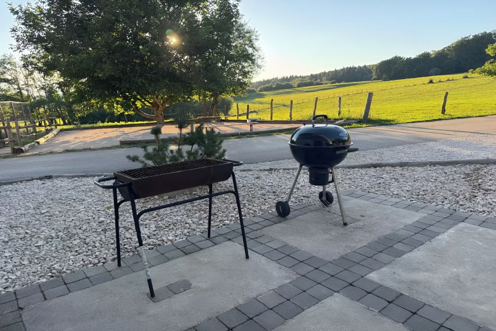 Ein Außenbereich mit Grill und Sitzbank, umgeben von einem Kiesweg und einem Zaun.