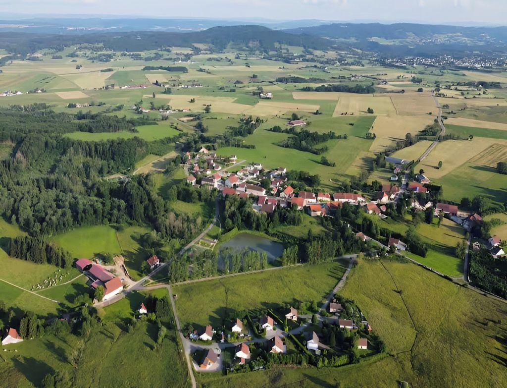 Een vogelvluchtperspectief van een landelijk dorp met huizen, velden en een klein waterlichaam.