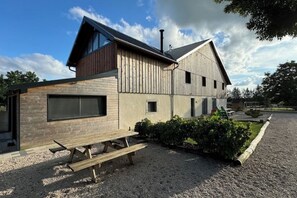 A modern house with a wooden exterior, a large window, and a gravel driveway. - Cosy cottage with relaxing view and outdoor barbecue (Laviron)