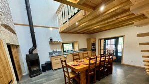 A spacious dining area with a wooden table and chairs, a kitchen with a window, and a loft with wooden beams. - Cosy cottage with relaxing view and outdoor barbecue (Laviron)