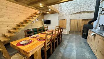 Une table à manger en bois avec des chaises, un escalier, un mur en pierre et une cheminée.