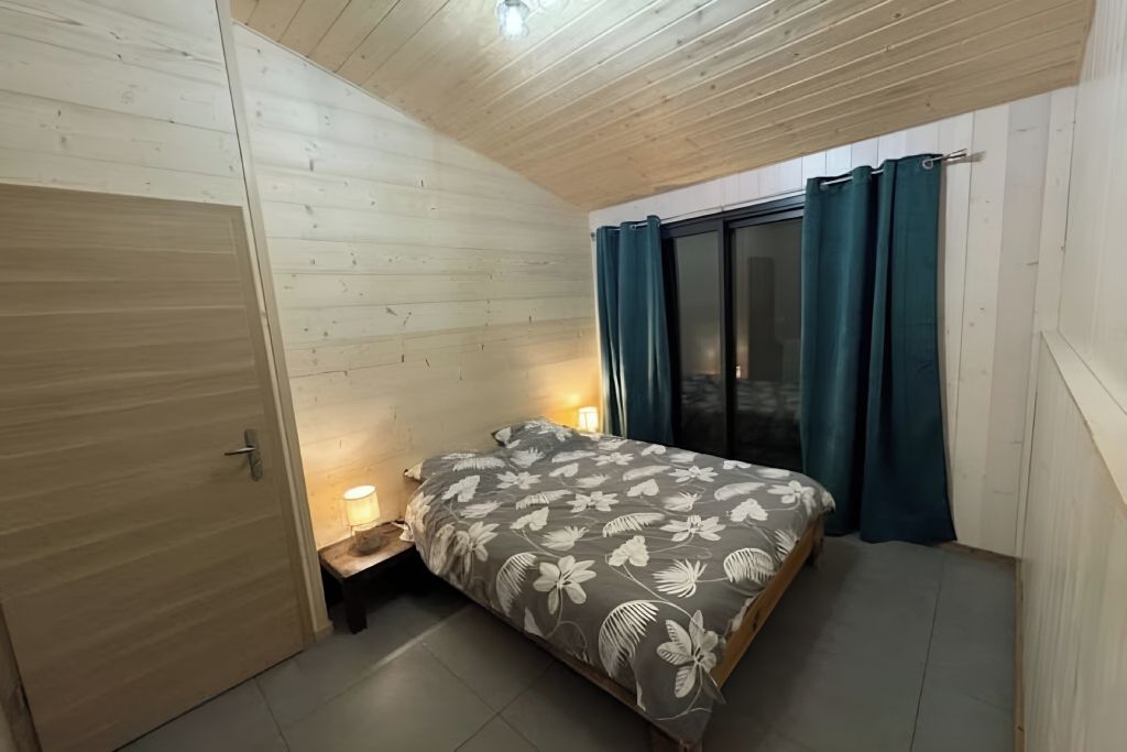 Un dormitorio con una cama, una mesita de noche, una ventana con cortinas y un techo de madera.