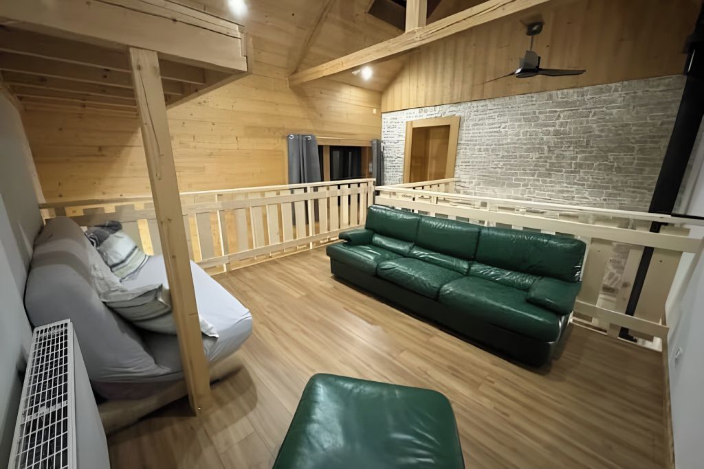 A cozy room with a green sofa, a bed with a mattress and pillows, a wooden ceiling, and a brick wall. - L'Éden – A 4-star vacation rental measuring 90 m² in the heart of a 3-hectare estate, accommodating 8 guests (Laviron)