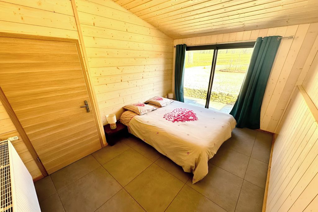 A wooden-paneled room with a bed, a window with curtains, and a door.
