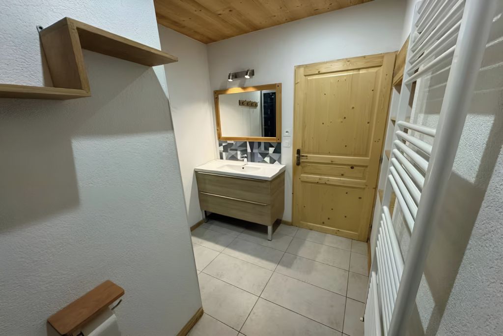 A bathroom with a wooden door, a sink with a mirror, and a towel rack.