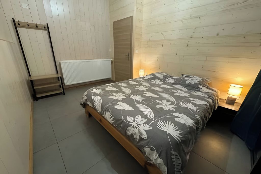 Un dormitorio con una cama, una mesita de noche, un radiador fijado a la pared y una puerta.