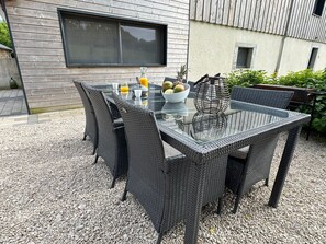 An outdoor dining area with a glass-top table and wicker chairs, set on a gravel surface. - Cosy cottage with relaxing view and outdoor barbecue (Laviron)