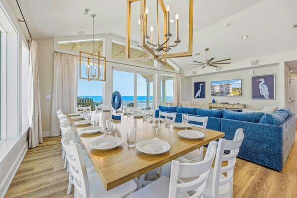 A dining area with a wooden table set for six, white chairs, and a blue sofa in the background.