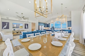 A spacious dining area with a long wooden table set for six, surrounded by white chairs.
