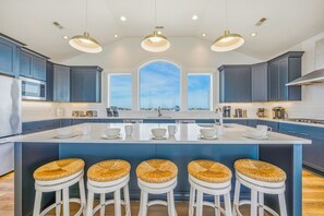 A modern kitchen with a central island, bar stools, and a view through the window.
