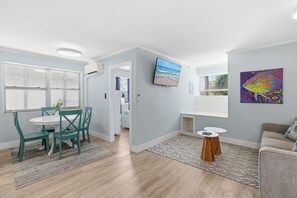 A modern living room with a dining area, a flat-screen TV, and artwork on the walls. - Flagler Ave 1 Bedroom/1 Bath-Eat, Drink, Play! (New Smyrna Beach)