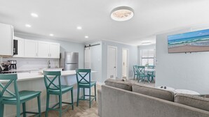 A modern kitchen with white cabinets, teal chairs, and a gray sofa.