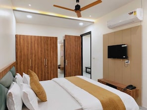 A hotel room with a bed, wooden wardrobe, a television, and an air conditioning unit.