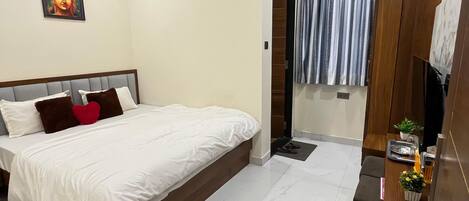 Une chambre moderne avec un grand lit, un ventilateur de plafond, un appareil de climatisation, une petite table avec une plante et une salle de bain avec un rideau de douche.