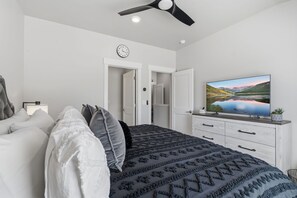 A modern bedroom with a bed, a television, and a ceiling fan.