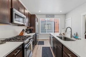 A modern kitchen with a central island, stainless steel appliances, and a 'GATHER' sign above a window.