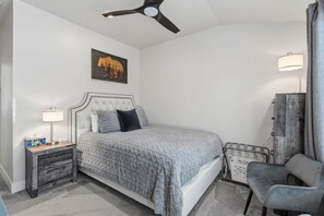 A bedroom with a bed, a nightstand, a lamp, a chair, a ceiling fan, and a wall-mounted cabinet.