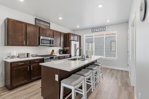 A modern kitchen with dark wood cabinets, stainless steel appliances, a central island with bar stools, and a window with blinds.