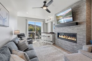 A modern living room with a fireplace, a ceiling fan, and a large TV mounted on the wall.