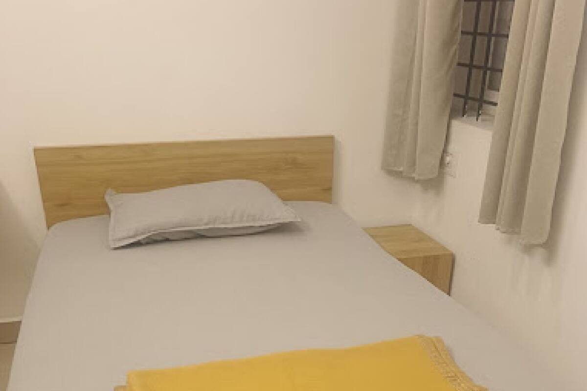 Un lit avec une tête de lit en bois, un oreiller blanc et une couverture jaune.