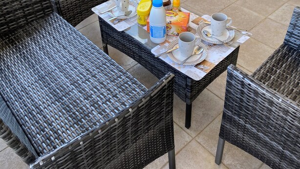 Un balcón con muebles de mimbre, una mesa con tazas, una botella y una bolsa de papas.