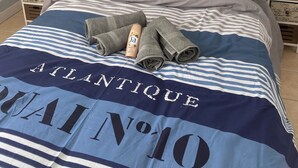 Una cama bien hecha con ropa de cama a rayas, una botella de loción y toallas dobladas.