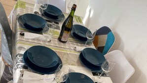 Mesa dispuesta para seis con platos azules, copas de vino y una botella de vino, cubierta con un mantel decorado con un diseño de bambú.