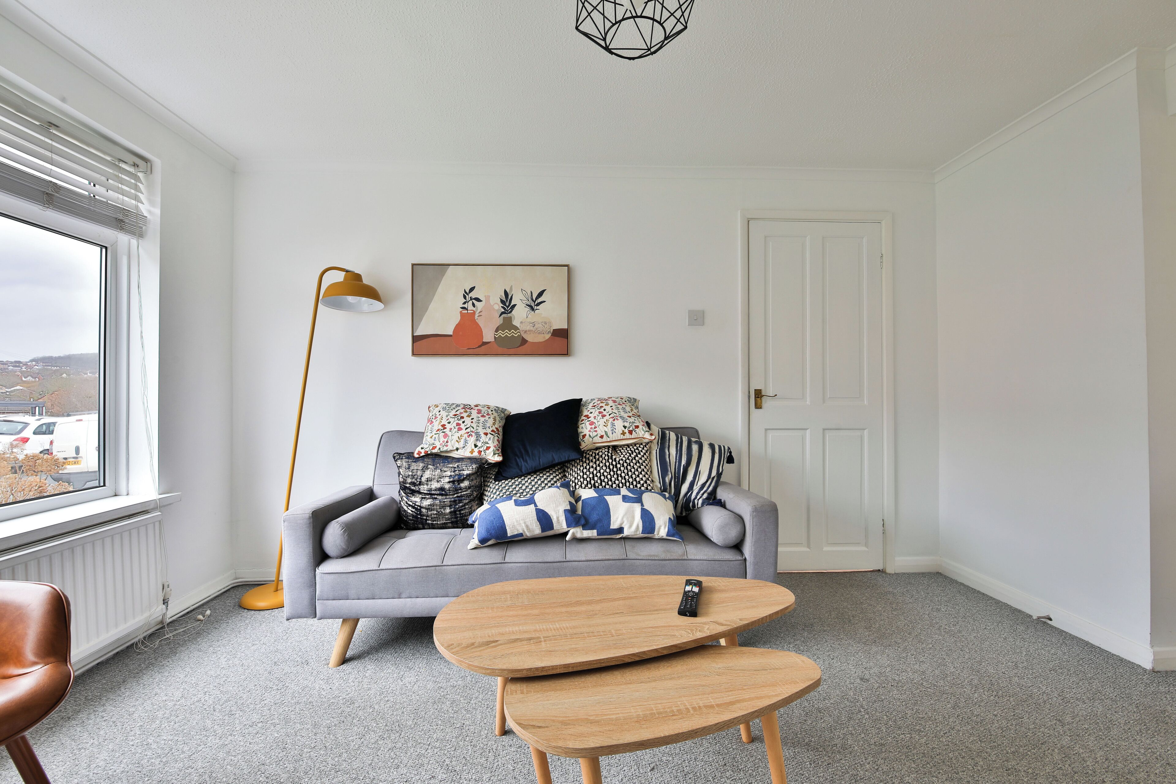 Un salon moderne avec un canapé gris, une table basse en bois, un lampadaire et un tableau accroché au mur.