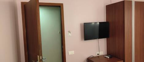 Una habitación con un armario de madera, un televisor montado en la pared y una puerta que da a otra habitación.