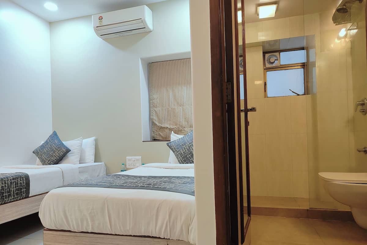 A hotel room with two beds, a window with blinds, an air conditioning unit, and a toilet.