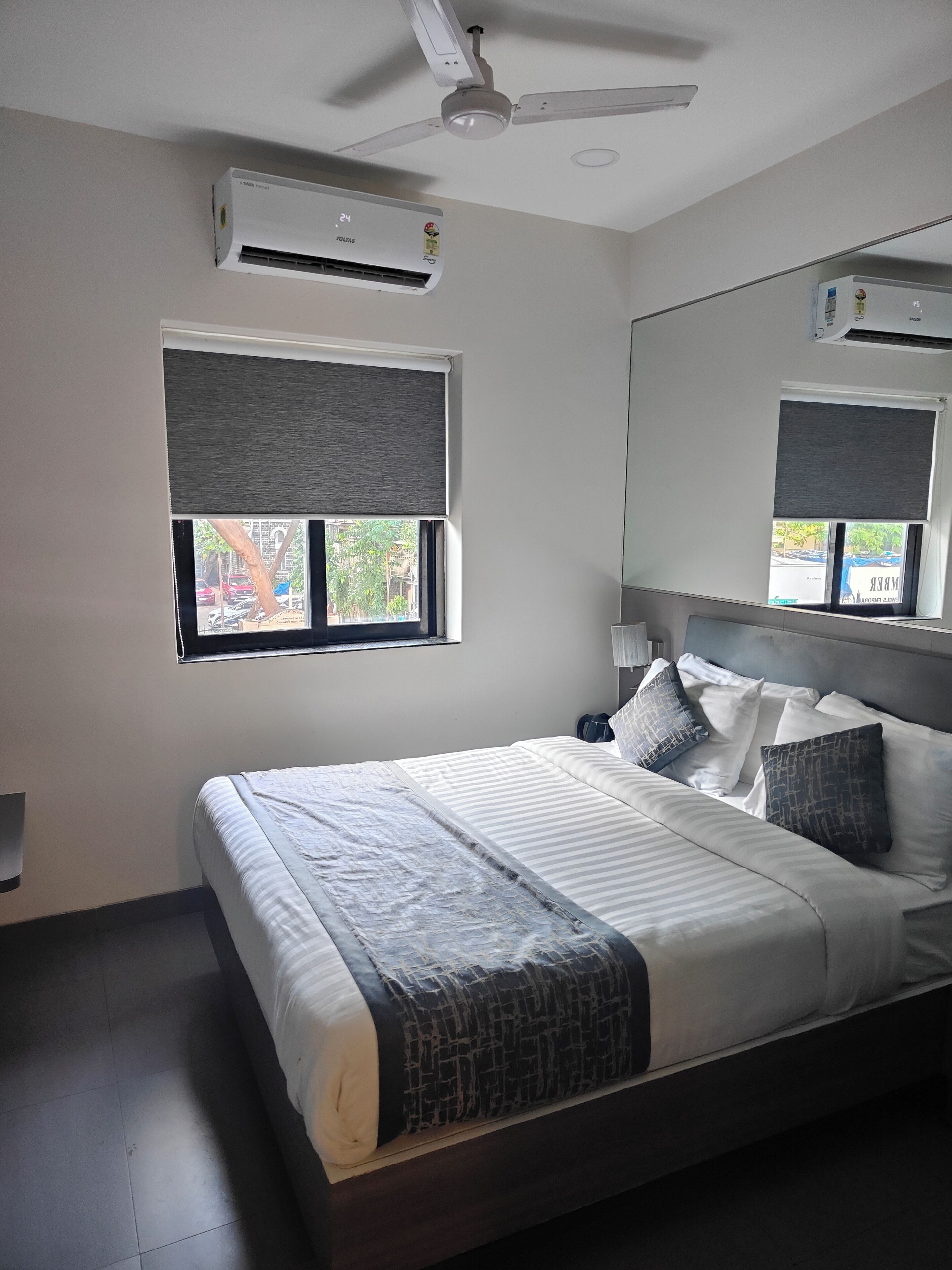Una camera da letto con un letto, un ventilatore a soffitto, un condizionatore d'aria, una finestra con vista e uno specchio.