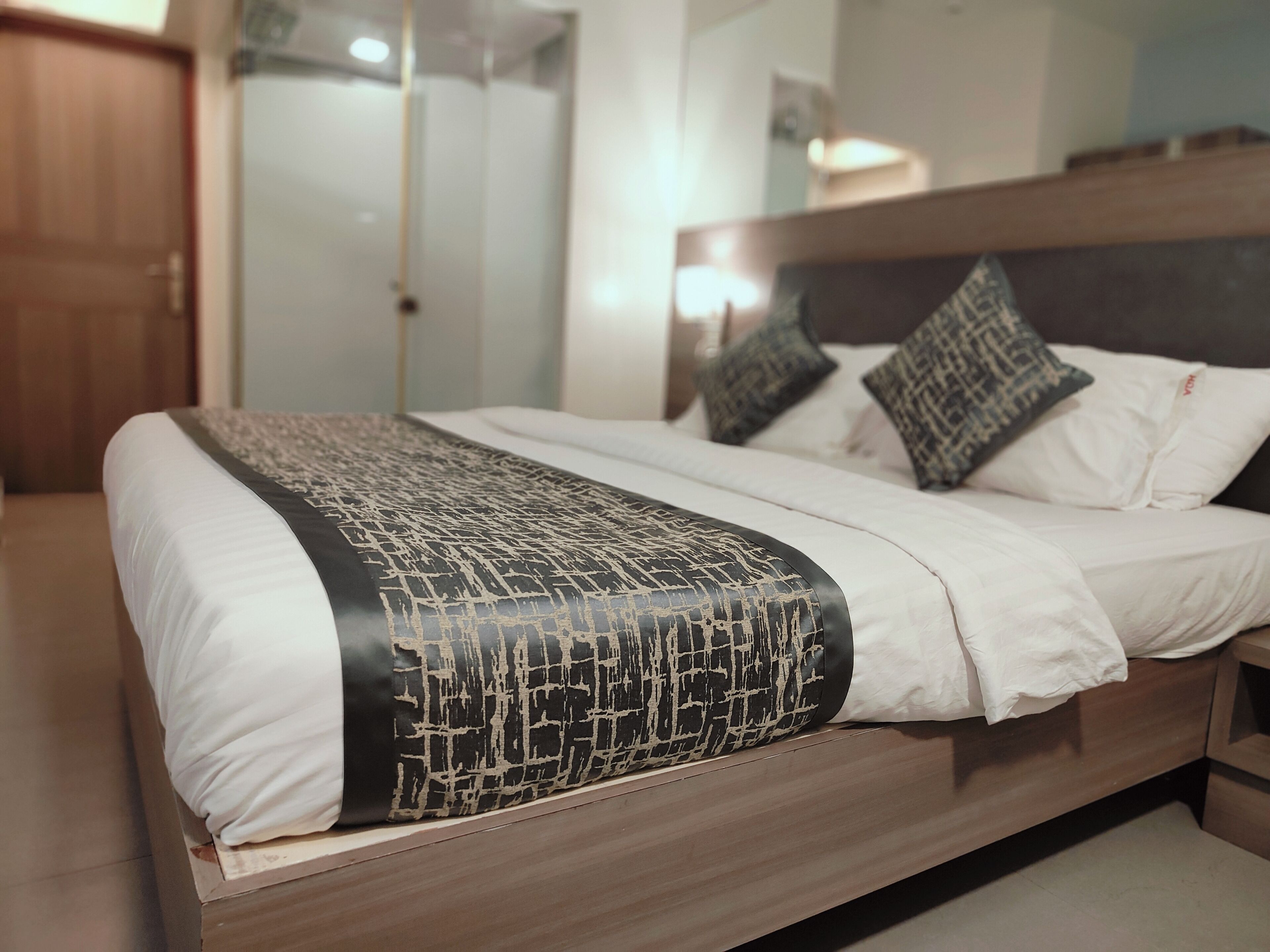 A neatly made bed with a patterned throw, white bedding, and two decorative pillows.